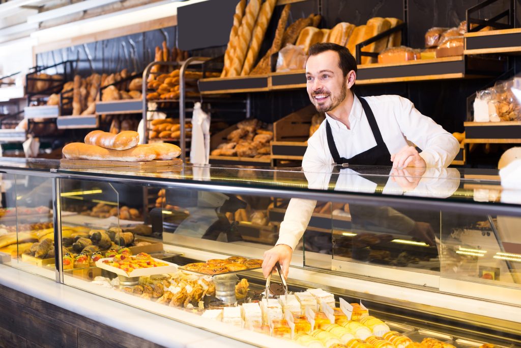 happy english male shop assistant demonstrating fresh delicious pastry in bakery